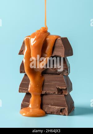 Verser la sauce caramel sur une pile de morceaux de chocolat.Morceaux de chocolat au lait et sauce caramel fondue isolés sur fond bleu. Banque D'Images