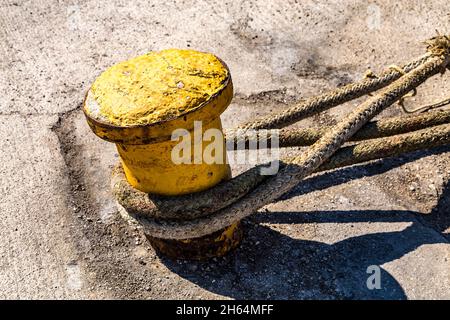 Vieux bollard jaune d'amarrage avec des cordes d'amarrage de service lourd sur une berth. Banque D'Images