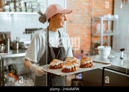 Jolie femme boulanger tient de beaux croissants avec de la crème brûlée d'albumine dans le magasin Banque D'Images