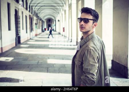 Beau jeune homme extérieur portant une veste et des lunettes de soleil, sous colonnade Banque D'Images
