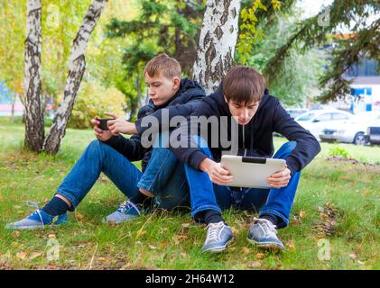 Sad Boys with Gadgets s'assoient sous un arbre dans le parc d'automne Banque D'Images