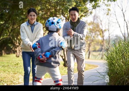 parents asiatiques aimant enseignant le patinage à roulettes à l'extérieur dans le parc de la ville Banque D'Images