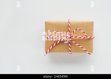 Boîte cadeau de Noël emballée dans du papier artisanal avec noeud à ficelle rayé rouge et blanc sur fond blanc.Vue de dessus, plat, espace de copie. Banque D'Images