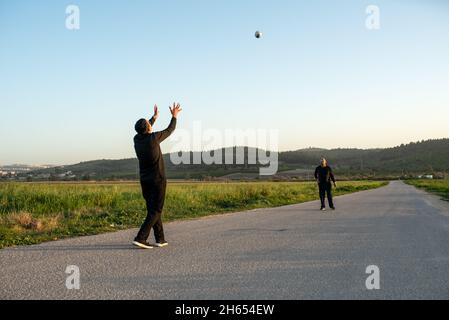 Un père âgé jette une balle dans l'air et un fils adolescent se prépare à l'attraper.Père senior et fils adolescent jouant avec le handball sur la nature au coucher du soleil le jour d'été.Une vraie famille s'amuser. Banque D'Images