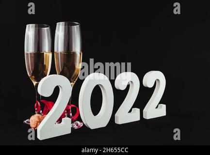 Sur fond noir, il y a deux verres en cristal avec champagne, un ruban rouge et un bouchon en liège.Devant elle se trouve le numéro 2022 en blanc. Banque D'Images