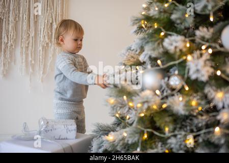 Adorable petite fille assise près de l'arbre de Noël avec des lumières festives et des cadeaux de Noël.Chrismas et le nouvel an. Banque D'Images