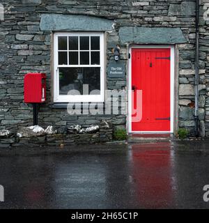 Le vieux Posthouse dans le joli village de Rosthwaite Lake District, Cumbria, Angleterre, Royaume-Uni, avec une porte rouge reflétée sur la route humide Banque D'Images