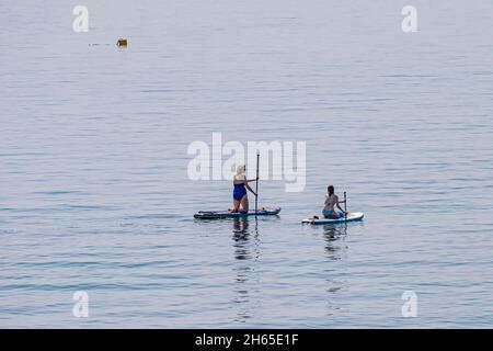 Deux femelles paddleboard sur un très calme, chaud jour de juillet, près de Charlestown, sud de Cornwall, Royaume-Uni. Banque D'Images