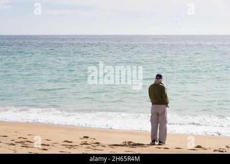 Arrière de l'homme solitaire senior pêche sur la plage.Personne aînée anonyme tenant la barre au bord de la mer.Concept de joie de retraite Banque D'Images