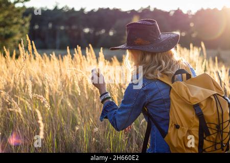 Une femme touristique avec chapeau et sac à dos profite d'une journée ensoleillée dans la nature.Détente à l'extérieur.La beauté dans la nature.Blonde cheveux femme portant des vêtements décontractés Banque D'Images