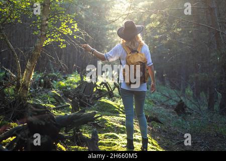 Femme avec chapeau et sac à dos randonnée en forêt.Le voyageur se trouve à sunbeam, dans la forêt.Femme touriste marchant à l'extérieur Banque D'Images