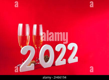 Sur fond rouge, il y a deux verres en cristal avec champagne, un cône de pin et un bouchon en liège.Devant elle se trouve le numéro 2022 en blanc. Banque D'Images