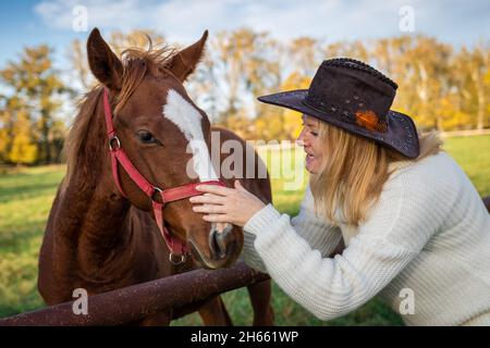 Femme jouant avec son jeune cheval au pâturage.Cowgirl aime son poulain.Amitié entre les personnes et les animaux domestiques.Femme portant un chapeau de cow-boy et un kni Banque D'Images