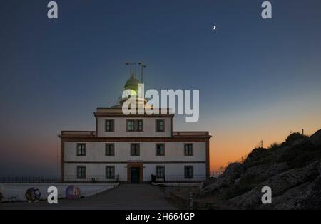 Feu vert au phare de Fisterra pendant la Lune du croissant, Galice, Espagne Banque D'Images