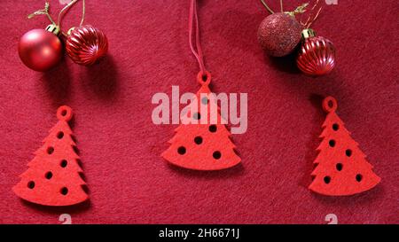 Jouet arbre de Noël en feutre rouge en forme d'arbre de Noël.Trois arbres de Noël sur fond rouge avec des boules de Noël.Nouvelle année. Banque D'Images