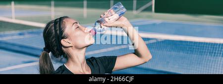 Thirsty Sporty Asian fille boire de l'eau tout en jouant au tennis sur le court extérieur.Sports active style de vie femme hydratant avec bouteille de sports nautiques Banque D'Images