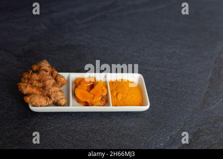 curcuma en trois présentations racine laminée et en poudre sur une plaque blanche et sur un fond noir Banque D'Images