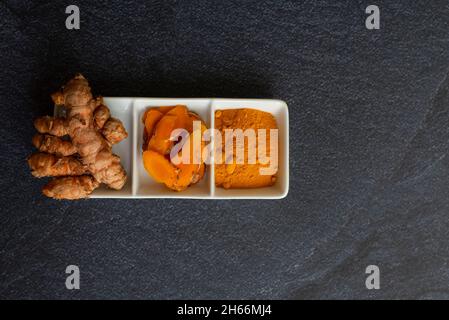 curcuma en trois présentations racine laminée et en poudre sur une plaque blanche et sur un fond noir Banque D'Images