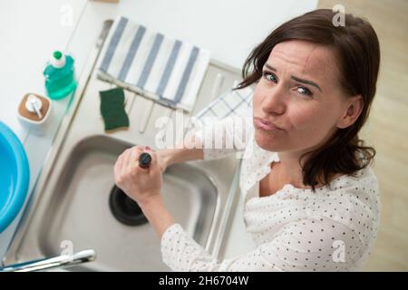 Jeune femme en utilisant le poussoir bloqué pour déboucher l'évier