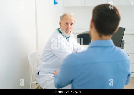 Vue rapprochée du dos à l'adulte adulte homme médecin portant un manteau blanc consultant jeune homme malade ou chirurgical méconnaissable. Banque D'Images