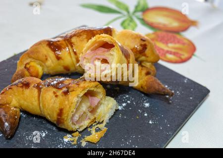 croissants frais farcis au jambon et au fromage fondu, prêts à manger, sur une assiette en ardoise grise Banque D'Images