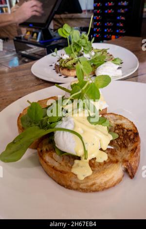 Œufs benedict et purée d'avocat sur pain grillé au levain, deux plats sont apportés à la table pour le petit déjeuner Banque D'Images