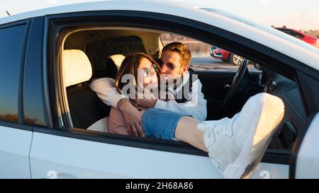 Touristes amoureux et insouciants couple de voyageurs assis en voiture au coucher du soleil dans la campagne.L'homme embrasse et embrasse sa petite amie tout en s'arrêtant en voyage.Voyage, voyage sur route et concept confortable Banque D'Images