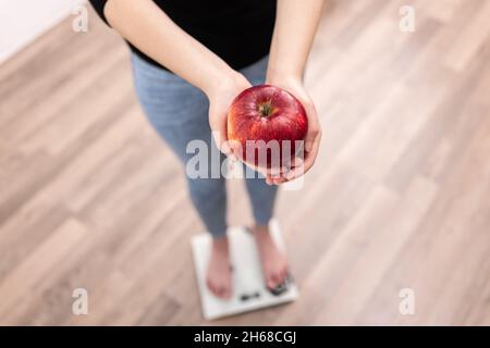 Une femme mesure le poids sur une balance, tient une pomme dans ses mains. Banque D'Images