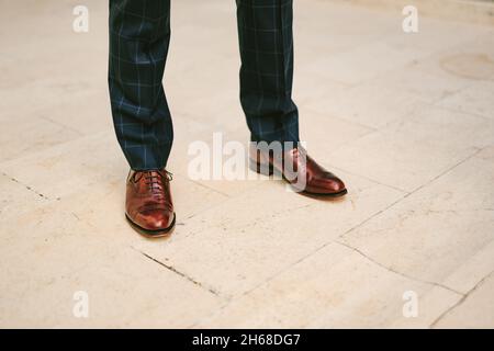 Homme dans un pantalon à carreaux noir et des chaussures en cuir verni marron se tient sur un sol carrelé.Jambes rapprochées Banque D'Images