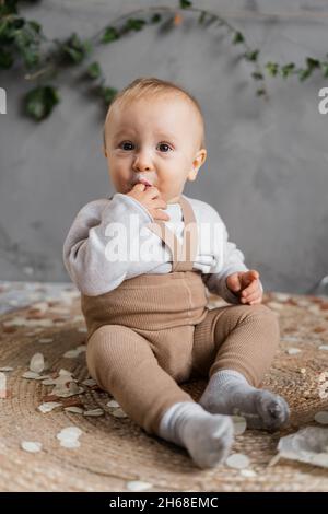 Portrait d'un tout-petit d'un an assis sur le sol, léchant son doigt de crème.Premier anniversaire d'un tout-petit. Banque D'Images