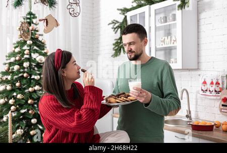 Un mari et une femme heureux avec des biscuits de Noël et du lait dans la cuisine. Banque D'Images