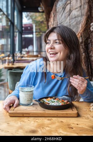 Une jeune femme dans un café dines sur le shakshuka traditionnel et ayran. Banque D'Images