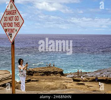 Honolulu, Hawaii - 6 novembre 2021-personnes se tiennent sur la plage des rochers au-delà du danger ne pas aller au-delà de ce point signe. Banque D'Images