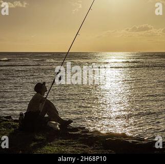 Honolulu, Hawaï - 6 novembre 2021 - Silhouette de pêche d'homme de la côte au coucher du soleil. Banque D'Images