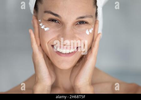 Portrait d'une jeune femme hispanique heureuse appliquant de la crème. Banque D'Images