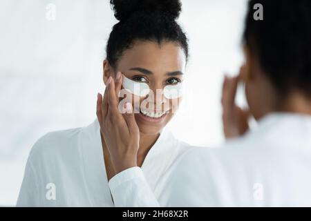 Jeune femme afro-américaine souriante appliquant des taches oculaires. Banque D'Images