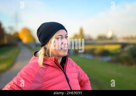 Femme d'âge moyen en bonnet dans un paysage d'automne au coucher du soleil en gros plan de la tête et des épaules alors qu'elle regarde sur le côté avec un sourire pensif Banque D'Images