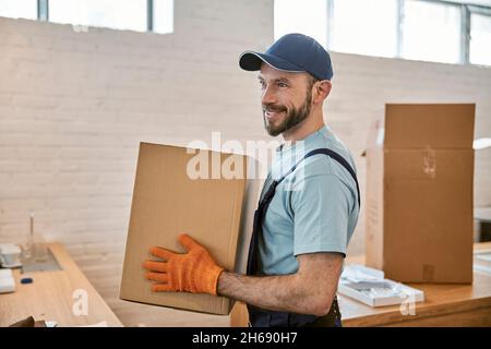 Homme barbu gai dans des gants tenant une boîte en carton Banque D'Images