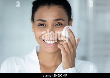 Bonne jeune femme afro-américaine qui nettoie le visage avec une éponge. Banque D'Images