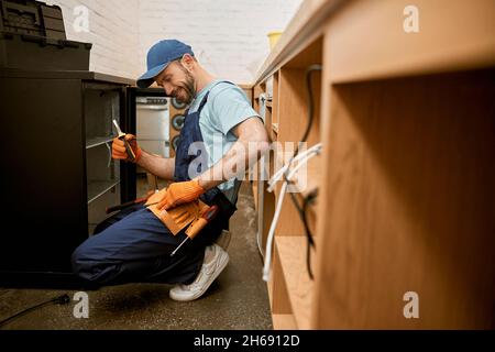 Joyeux jeune homme qui fixe le réfrigérateur dans la cuisine Banque D'Images