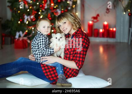 Famille de deux personnes mère et à la veille du nouvel an près de l'arbre de Noël décoré assis sur le sol avec un petit animal de compagnie. Banque D'Images