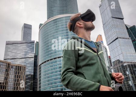 Moscou, Russie.21 août 2021 Un jeune homme portant des lunettes de réalité virtuelle est photographié au festival de la technologie de la science de pique-nique de Geek, dans le contexte des gratte-ciels du centre financier et des bureaux 'Moscow City' à Moscou, en Russie Banque D'Images