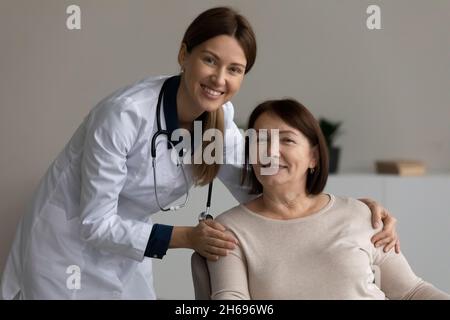 Prise de vue en tête portrait femme thérapeute souriante touchant les épaules des patients matures Banque D'Images