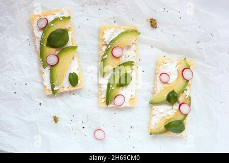 toasts croustillants sans gluten avec fromage doux, avocat, radis et basilic sur fond blanc, vue du dessus Banque D'Images