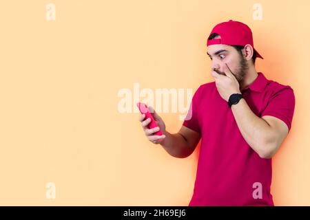 Un jeune homme a surpris tout en vérifiant son téléphone cellulaire; un fond orange avec un espace de copie Banque D'Images
