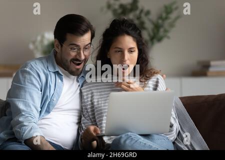Un jeune couple choqué et débordant de joie à regarder sur un ordinateur portable, à lire des nouvelles étonnantes Banque D'Images