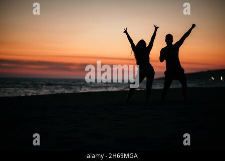 Une silhouette d'un couple fou posé sur une plage avec un fond de beau coucher de soleil. Banque D'Images