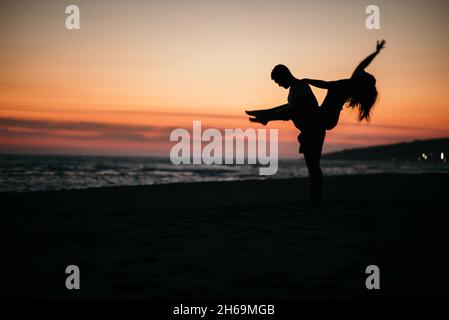 Une silhouette d'un couple fou posé sur une plage avec un fond de beau coucher de soleil. Banque D'Images