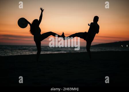 Une silhouette d'un couple fou posé sur une plage avec un fond de beau coucher de soleil. Banque D'Images