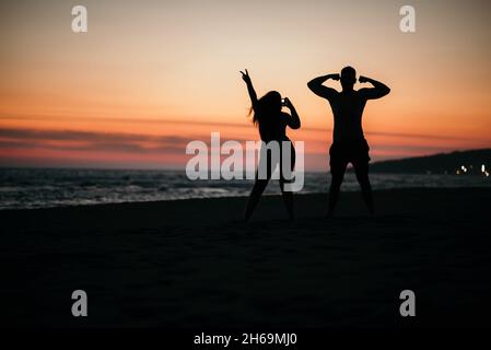 Une silhouette d'un couple fou posé sur une plage avec un fond de beau coucher de soleil. Banque D'Images